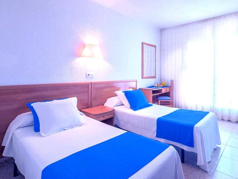 Camera d'hotel con due letti singoli, biancheria da letto blu e bianca, ambiente luminoso e accogliente.