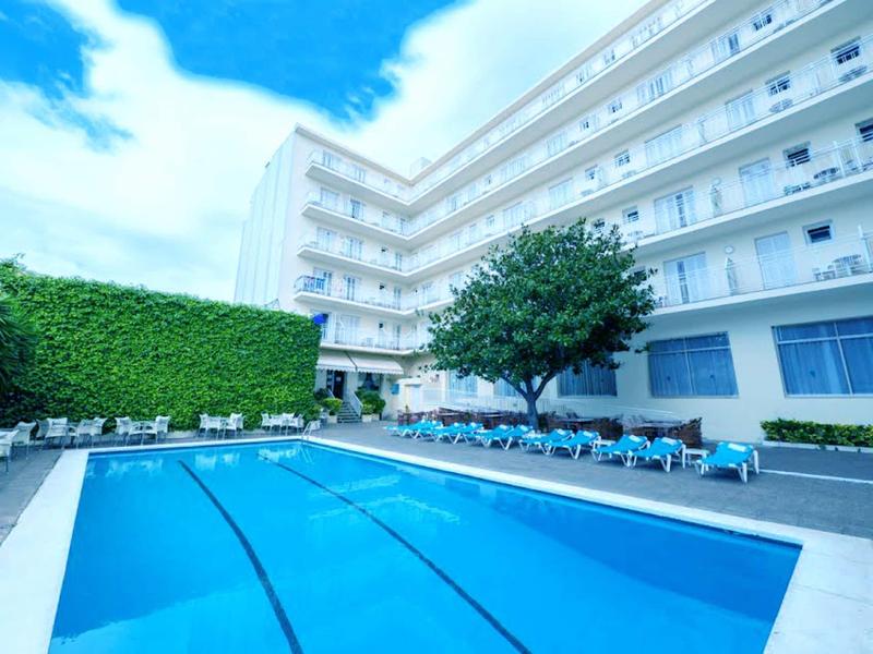 Piscina moderna dell'hotel con lettini e albero verde, circondata da edifici bianchi.