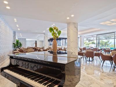 Hall d'hôtel moderne avec piano noir, espaces assis et grandes fenêtres.