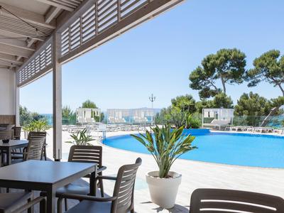 Piscine avec coin repas et vue sur la ville et la mer par ciel clair.