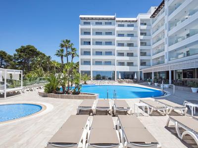 Espace piscine d'hôtel moderne avec chaises longues, palmiers et ciel bleu clair.