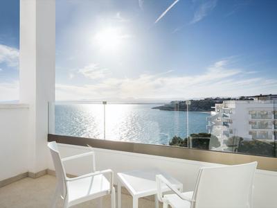 Balcon avec chaises blanches et table offrant une vue sur la mer sous un ciel ensoleillé.