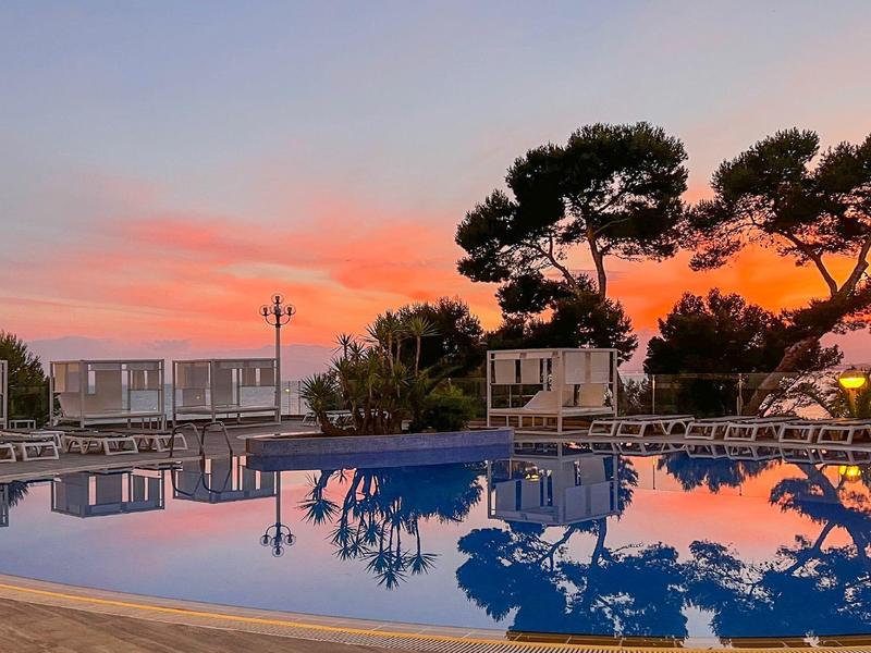 Piscine ronde au coucher du soleil reflétant des arbres et des nuages.