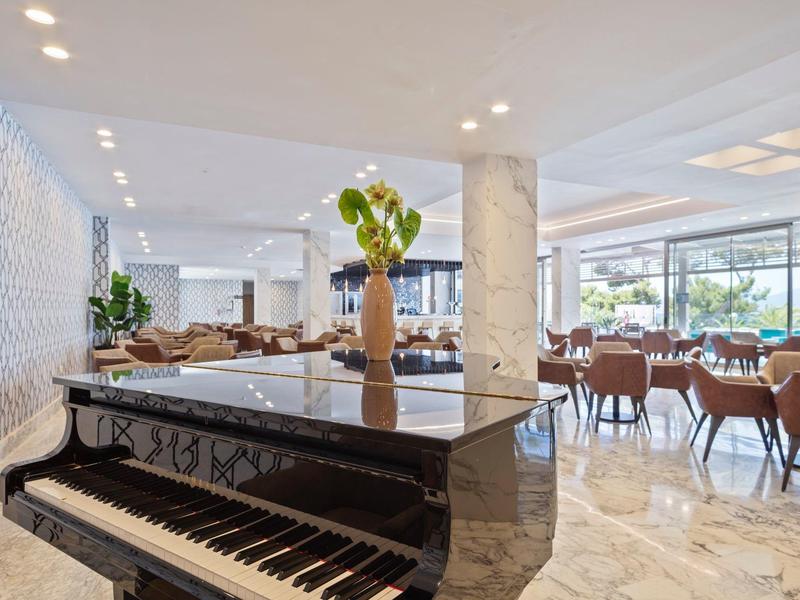 Hall d'hôtel moderne avec piano noir, espaces assis et grandes fenêtres.