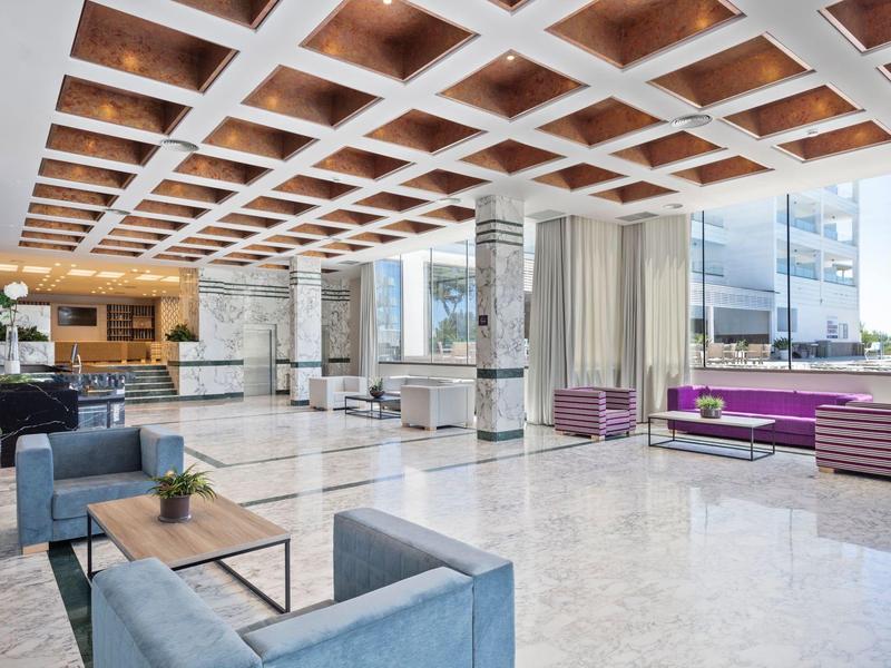 Grand hall d'hôtel avec sols en marbre, sièges modernes et panneaux de plafond en bois.
