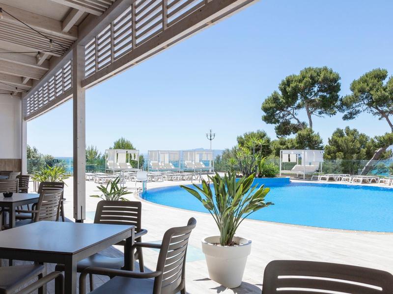 Piscine avec coin repas et vue sur la ville et la mer par ciel clair.