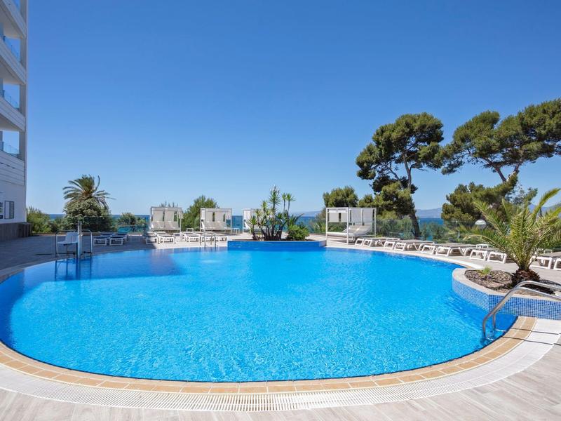 Piscine ronde d'hôtel avec chaises longues bleues et ciel bleu clair, entourée de palmiers.