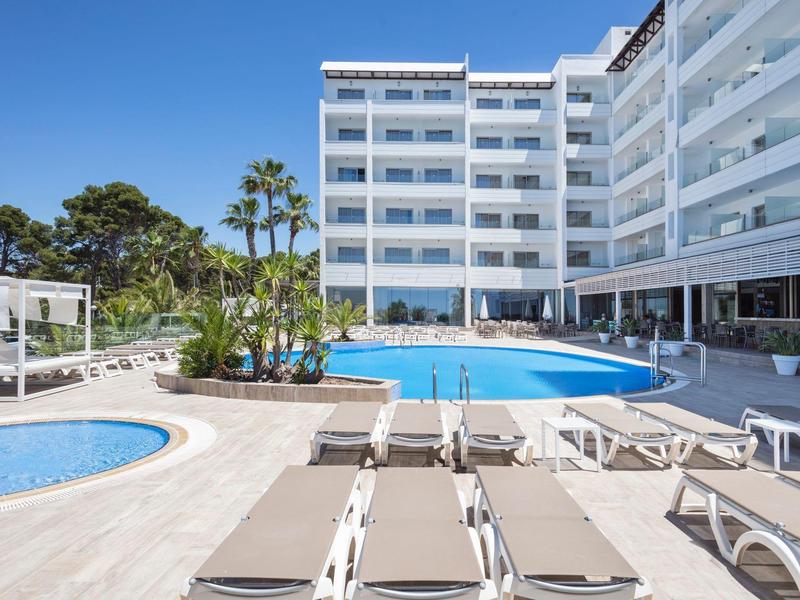 Espace piscine d'hôtel moderne avec chaises longues, palmiers et ciel bleu clair.