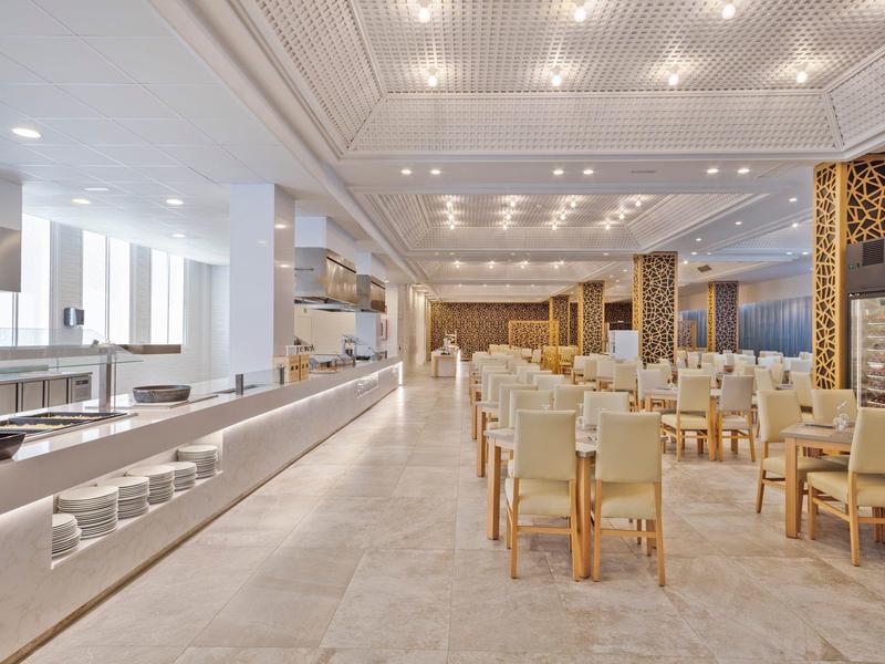 Salle à manger lumineuse et moderne avec chaises en bois et cuisine ouverte dans un hôtel.