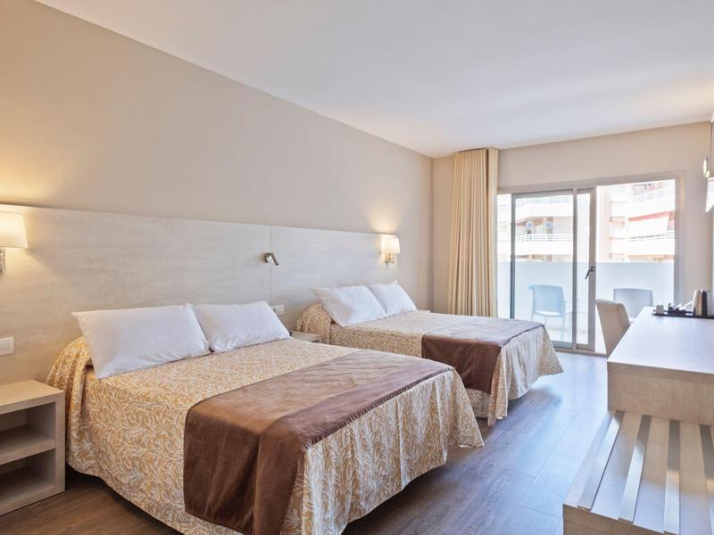 Chambre d'hôtel avec deux lits doubles, tables de chevet, téléviseur et balcon donnant sur l'extérieur.