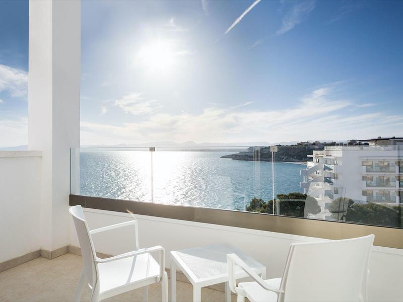 Balcon avec chaises blanches et table offrant une vue sur la mer sous un ciel ensoleillé.
