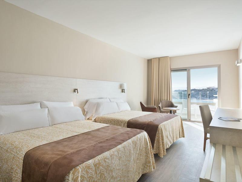 Chambre d'hôtel lumineuse avec deux lits, bureau, chaise et vue sur le balcon.