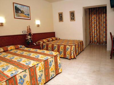 Pokój hotelowy z dwoma dużymi łóżkami, kolorowymi pościelami i prostym wyposażeniem.