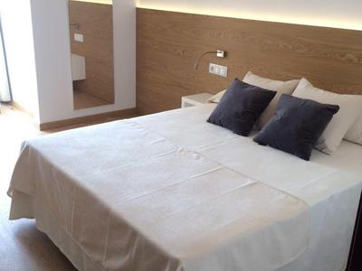 Jasna sypialnia z podwójnym łóżkiem, białą pościelą, ciemnymi poduszkami i dużym lustrem obok.