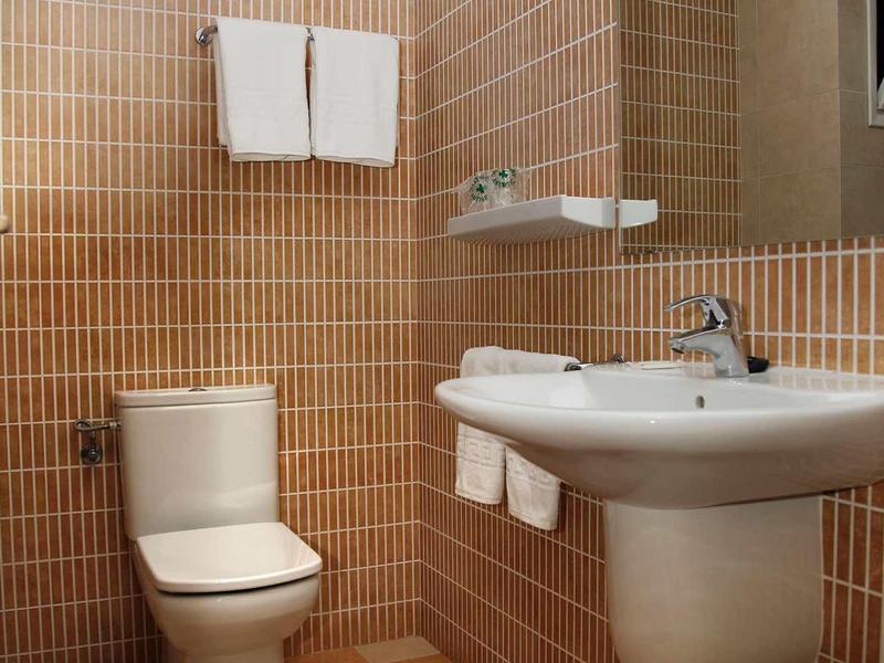 Mała łazienka hotelowa z toaletą, umywalką, lustrem i ręcznikami na haczykach.