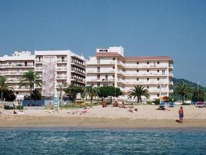 Wielopiętrowy hotel przy piaszczystej plaży z palmami i spokojnym morzem na pierwszym planie.
