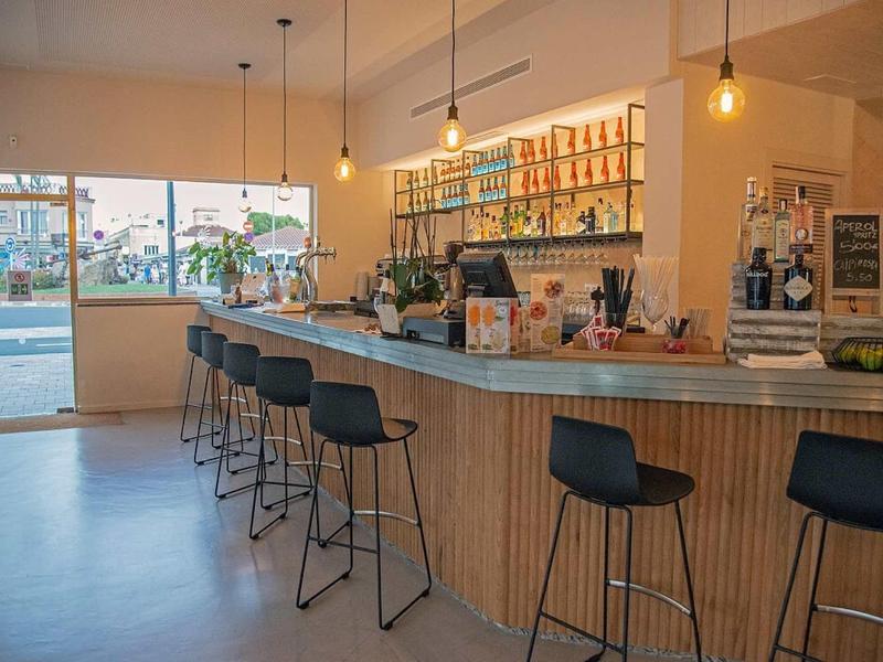 Nowoczesny bar hotelowy z drewnianym blatem, czarnymi hokerami i wiszącymi lampami.