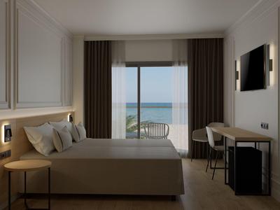 Modern hotel room with double bed, desk, and sea view through large windows.