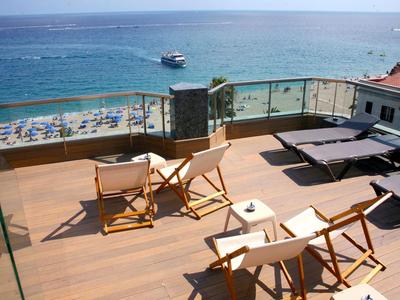 View from a rooftop terrace with chairs and loungers overlooking the sea and beach.
