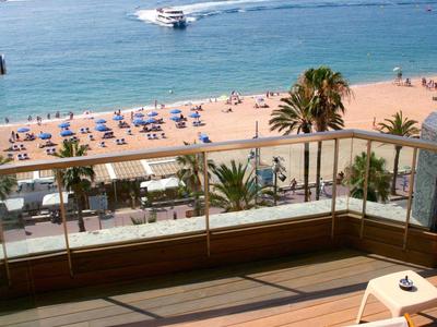 Balcony with wooden floor overlooking the beach and sea with umbrellas and boats.