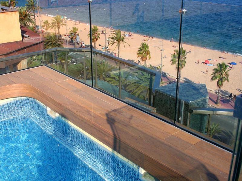 Modern pool overlooking the beach and blue sea under a clear sky.