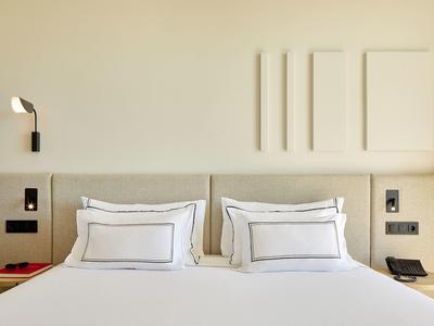 Moderní hotelový pokoj s manželskou postelí, bílými polštáři a minimalistickou stěnovou dekorací.