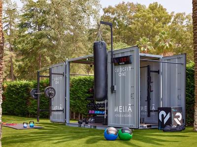 Kontejner přeměněný na venkovní fitness prostor s vybavením na zeleném trávníku.