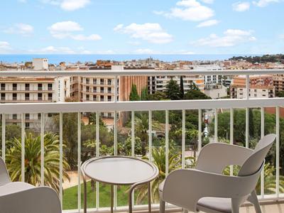 Balkon hotelu se dvěma židlemi a stolkem, výhled na město a moře v dálce.