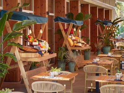 Gemütlicher Außenbereich mit Holzwänden, Pflanzen und gedeckten Tischen in einem Restaurant.