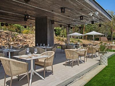 Venkovní terasa restaurace s stolky, židlemi z lana a bílými slunečníky.