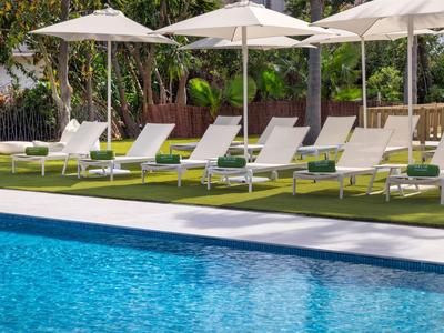 Rij ligstoelen met witte parasols naast een blauw buitenzwembad.