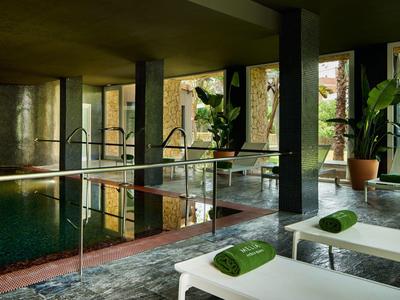 Poklidný vnitřní bazén s bílými lehátky a zelenými ručníky v moderním hotelu.