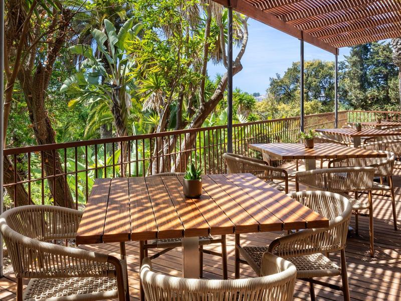 Zastíněná hotelová terasa s dřevěnými stolky a židlemi pod stříškou.