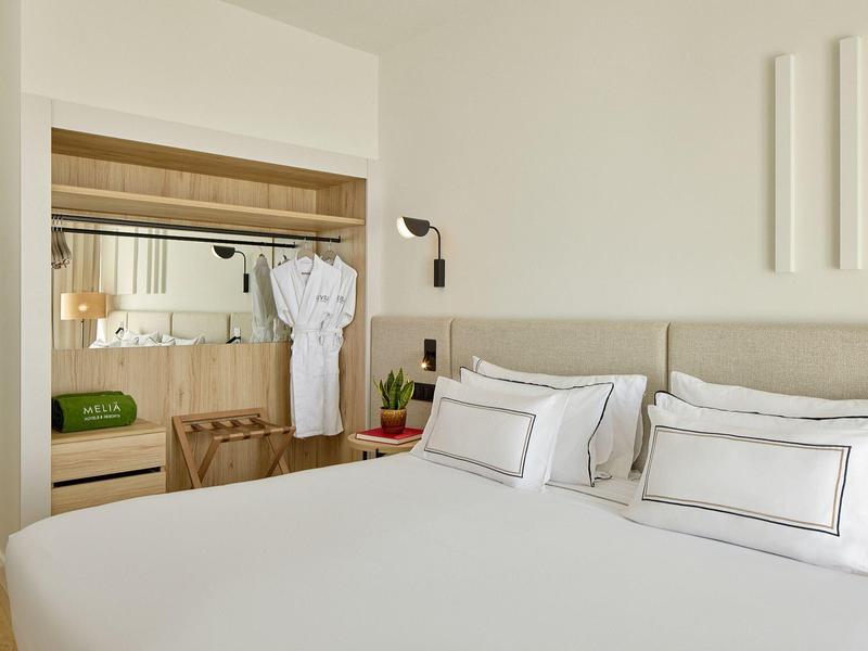 Moderní hotel s velkým bazénem, bílými lehátky a modrou oblohou s obláčky.