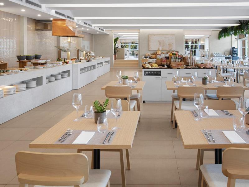 Moderní hotelová restaurace s dřevěnými stoly, připraveným nádobím a světlou atmosférou.