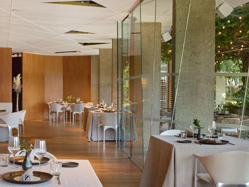 Elegantní jídelna s velkými skleněnými zdmi a teplým dřevěným nábytkem.