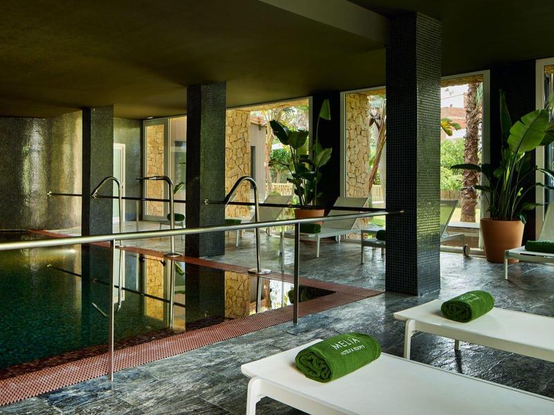 Poklidný vnitřní bazén s bílými lehátky a zelenými ručníky v moderním hotelu.