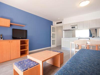 Soggiorno moderno con parete blu, mobili in legno e cucina aperta.