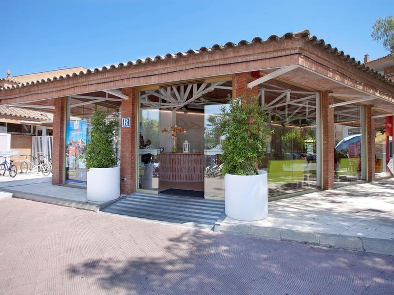 Area esterna di caffè con tetto in legno rustico e piante sotto un cielo azzurro chiaro.