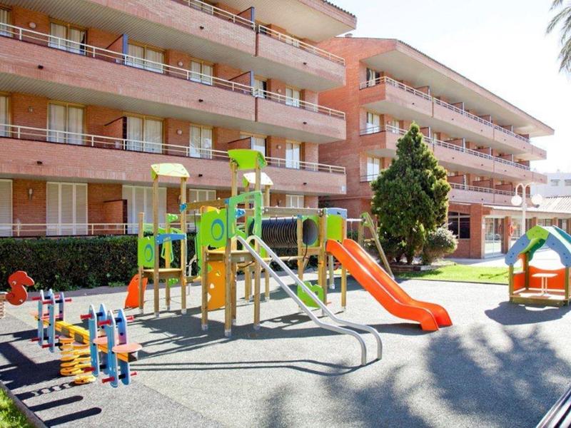 Area giochi con scivoli e strutture per arrampicarsi vicino a un edificio alberghiero alla luce del giorno.