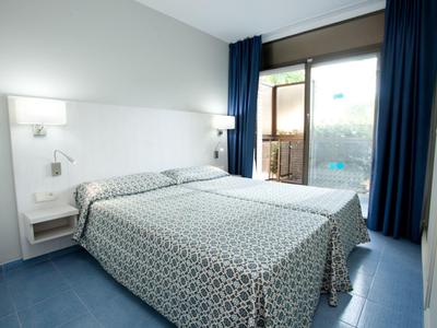 Chambre d'hôtel lumineuse avec lit double, tables de chevet et vue sur balcon avec piscine.