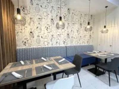 Restaurant moderne avec rangées de tables, chaises noires et éclairage mural décoratif.