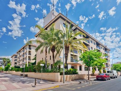 Immeuble résidentiel à plusieurs étages avec des palmiers et des voitures garées sous un ciel clair