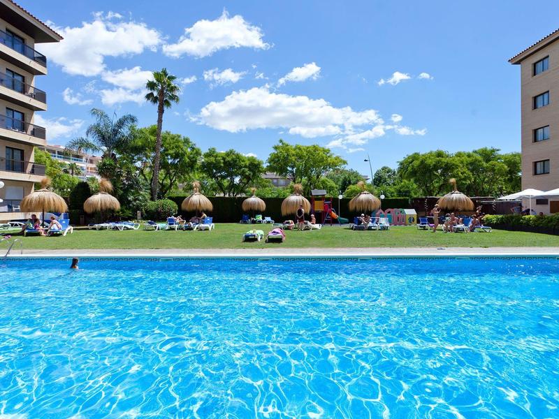 Piscine claire entourée de chaises longues et parasols entre deux bâtiments d'hôtel.