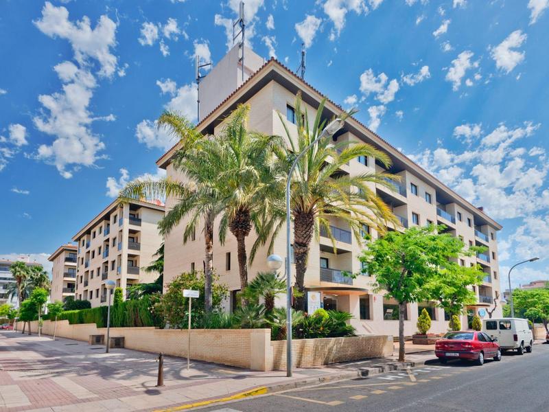 Immeuble résidentiel à plusieurs étages avec des palmiers et des voitures garées sous un ciel clair
