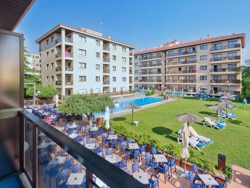Hôtel avec piscine, chaises longues et espace de restauration en plein air dans une cour verte.