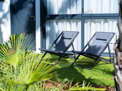 Deux chaises longues noires sur pelouse verte près d'une fenêtre.