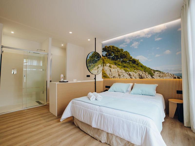 Nowoczesny pokój z łóżkiem podwójnym, szklaną łazienką i widokiem na słoneczne wzgórze.