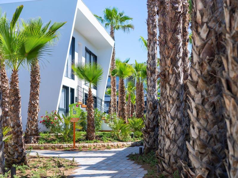 Ukośna ścieżka wyłożona płytkami otoczona palmami prowadząca do nowoczesnego białego budynku.