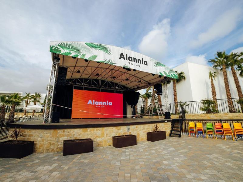 Zadaszona scena na zewnątrz z ekranem i kolorowymi krzesłami pod pochmurnym niebem.